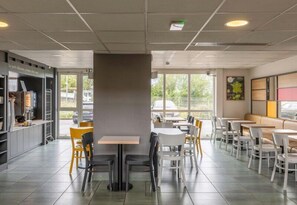 A modern cafe with tables and chairs, a counter with a menu, and large windows.