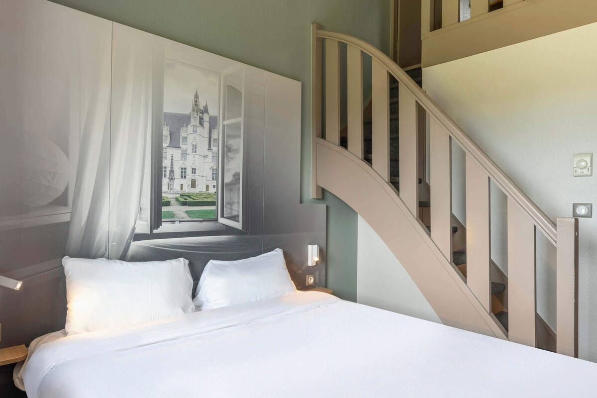 Un dormitorio con cama, mesita de noche, lámpara de pared y una escalera.