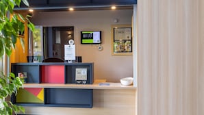 A reception desk with a digital screen, framed certificates, and a small bowl. - B&B HOTEL Rennes Est Cesson Sévigné 3 étoiles (Cesson-Sevigne)