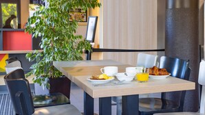 A breakfast table with a croissant, eggs, and orange juice, surrounded by chairs and a potted plant. - B&B HOTEL Rennes Est Cesson Sévigné 3 étoiles (Cesson-Sevigne)