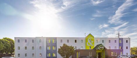 A multi-story hotel with a distinctive yellow and purple facade, a parking lot, and a clear sky.