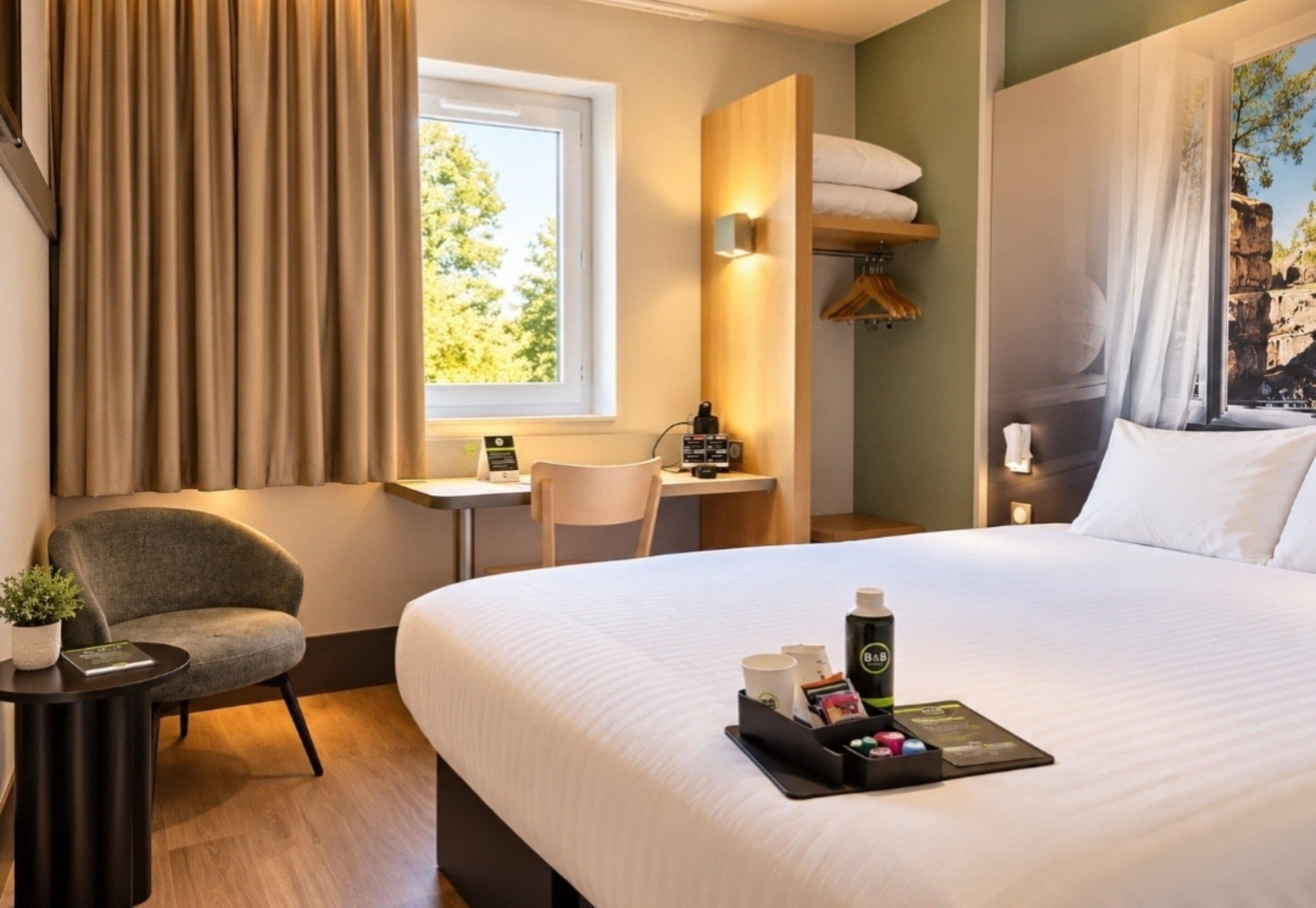 Habitación de hotel con cama, escritorio, silla, mesita y ventana con cortinas.