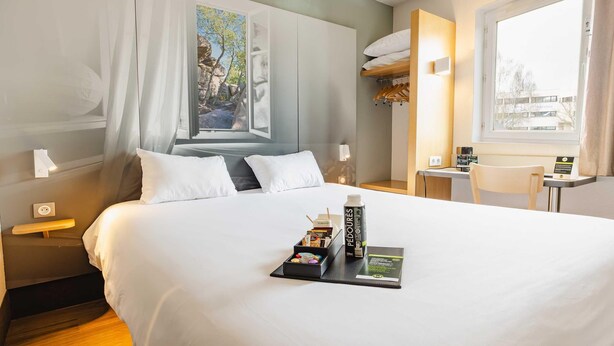 A hotel room with a bed, bedside table, lamp, window, and a desk with a chair. - B&B HOTEL Rennes Est Cesson Sévigné 3 étoiles (Cesson-Sevigne)