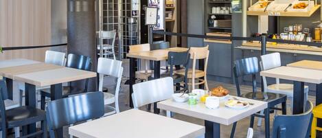 A restaurant with multiple tables and chairs, a counter with food items, and a menu board.