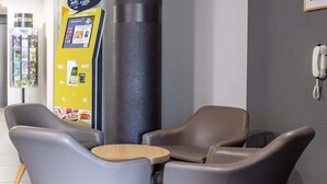 A seating area with two chairs and a small table, a self-service kiosk, and a telephone on the wall. - B&B HOTEL Rennes Est Cesson Sévigné 3 étoiles (Cesson-Sevigne)