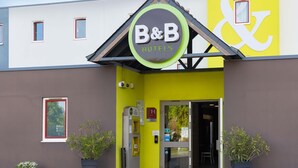 A B&B hotel entrance with a distinctive yellow and white facade, a visible entrance door, and a small window with a red frame. - B&B HOTEL Rennes Est Cesson Sévigné 3 étoiles (Cesson-Sevigne)