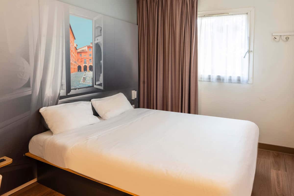 Una cama bien hecha en una habitación de hotel con vista a un edificio rojo a través de una ventana.