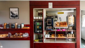 Een kitchenette met een koffieapparaat, planken met potten en een koelkast.