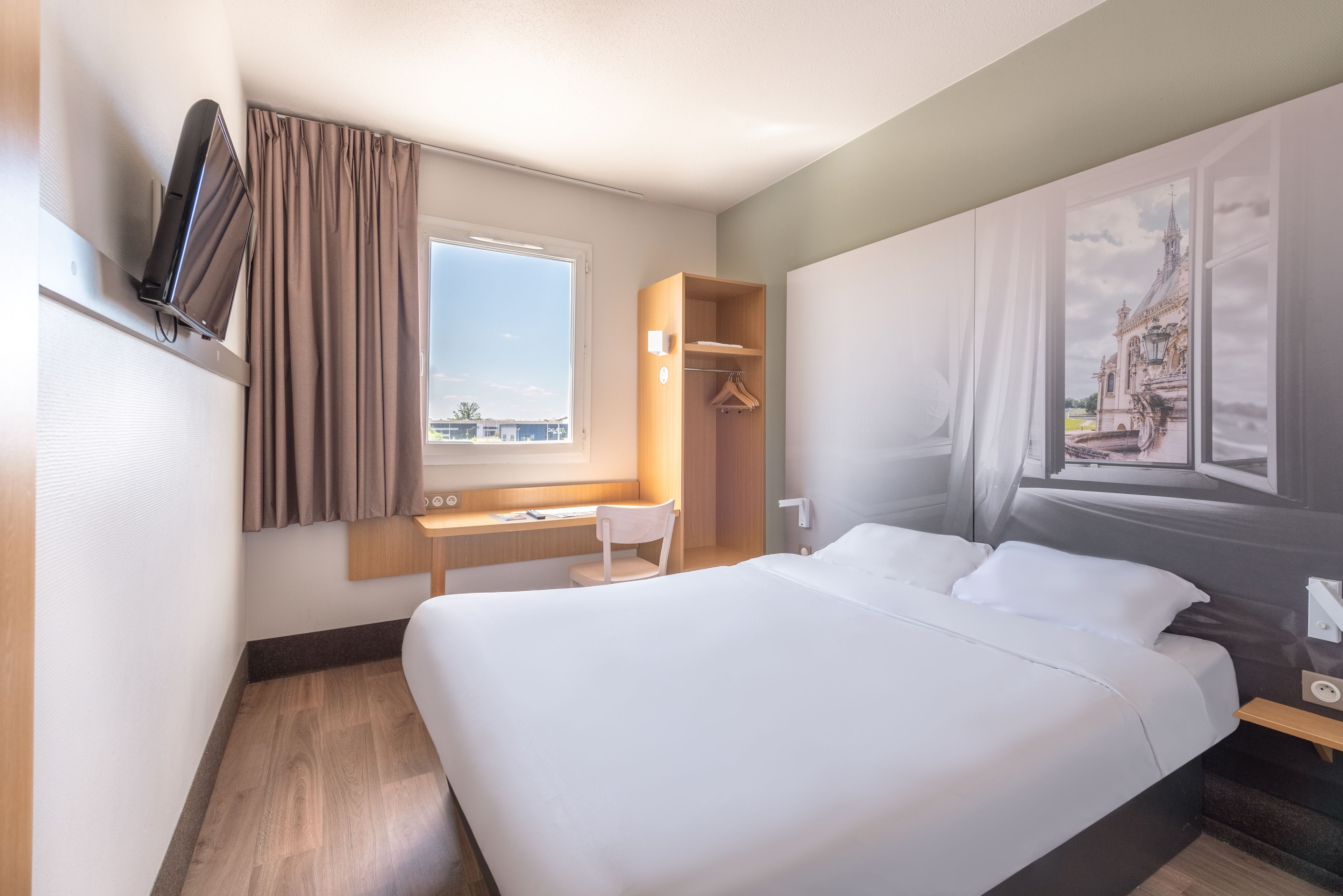 Een hotelkamer met een groot bed, een bureau, een stoel, een kledingkast en een raam met gordijnen.