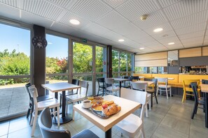 Um café com mesas e cadeiras, um relógio e vista para árvores lá fora.