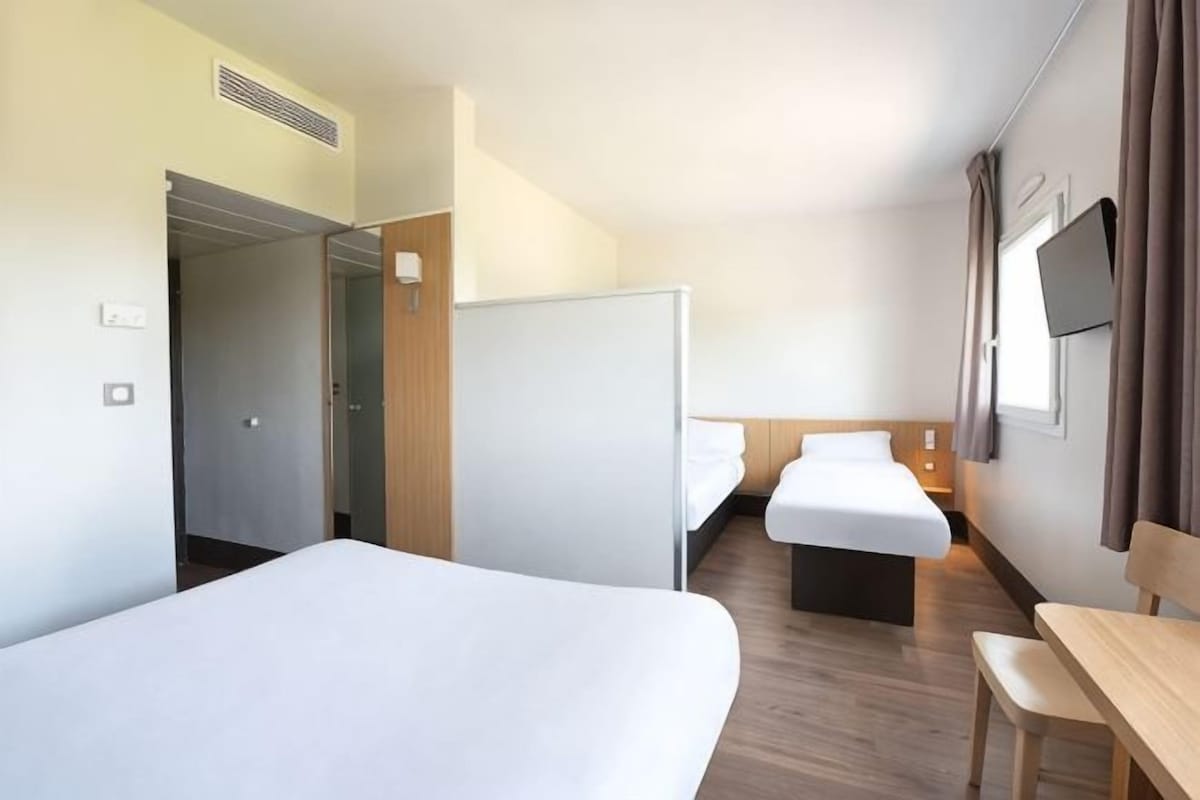 Habitación de hotel con dos camas, un escritorio, un televisor y una puerta que da a un pasillo.