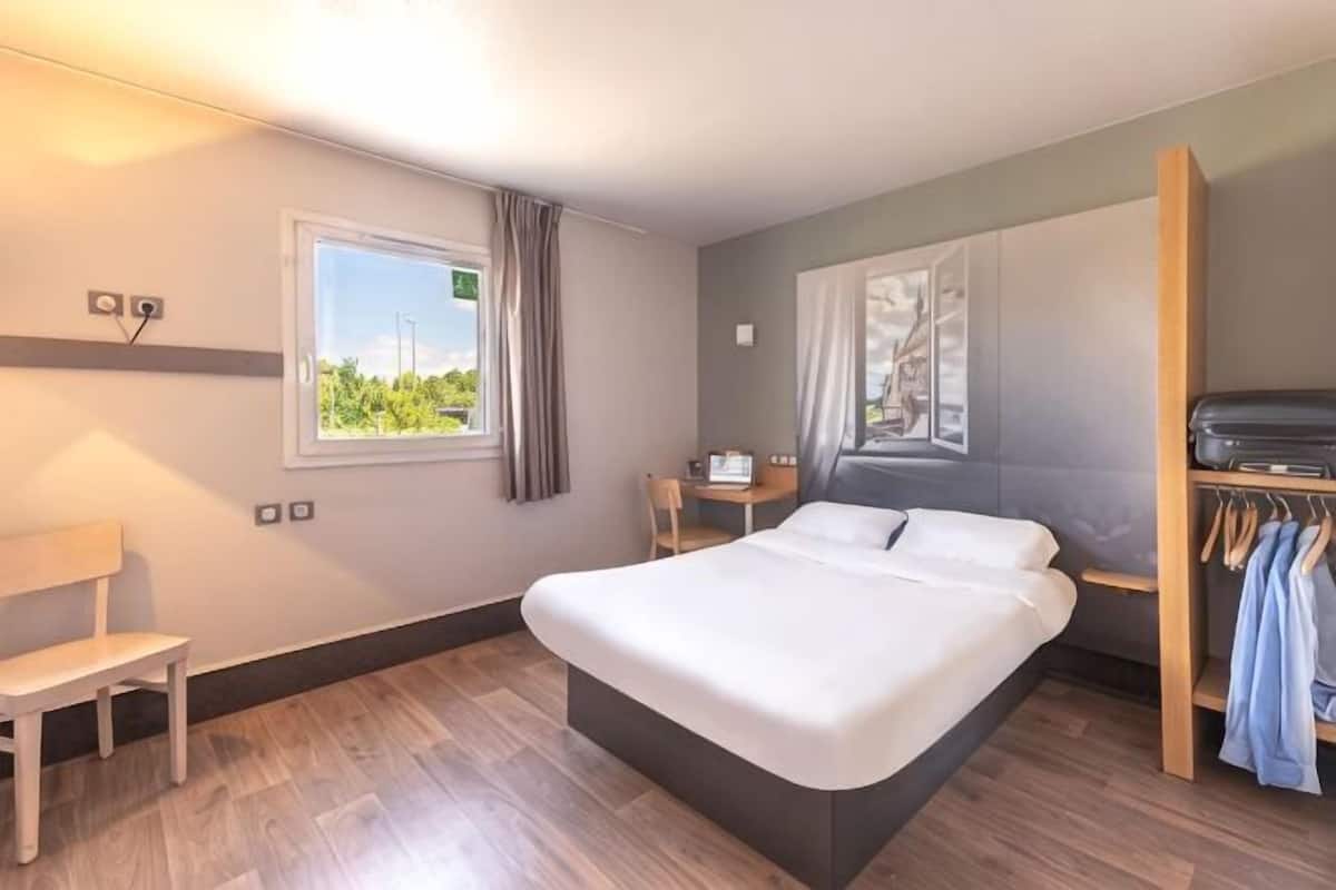 Een hotelkamer met een bed, bureau, stoel, kledingkast en raam met uitzicht.