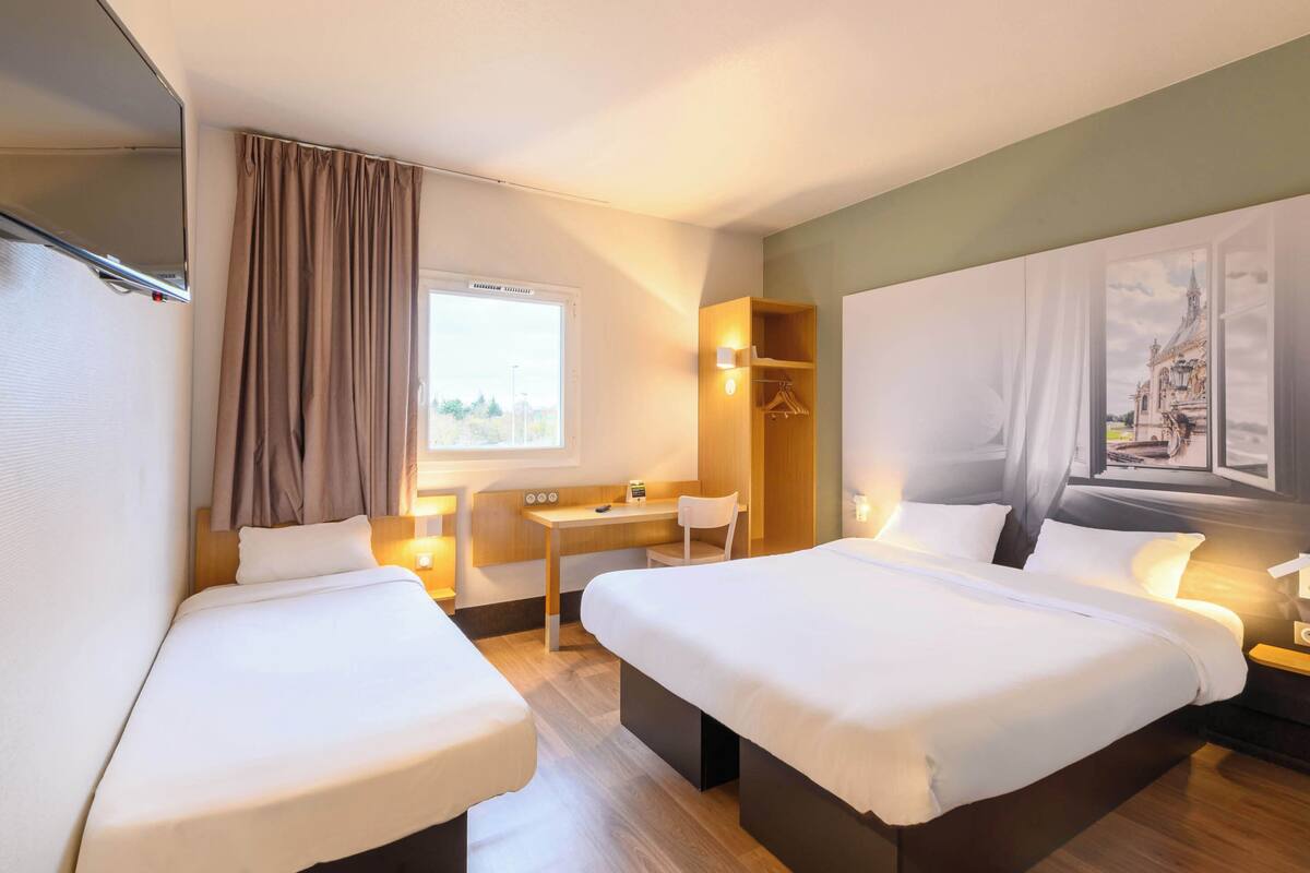 Een hotelkamer met twee bedden, een bureau, een stoel en een raam met gordijnen.