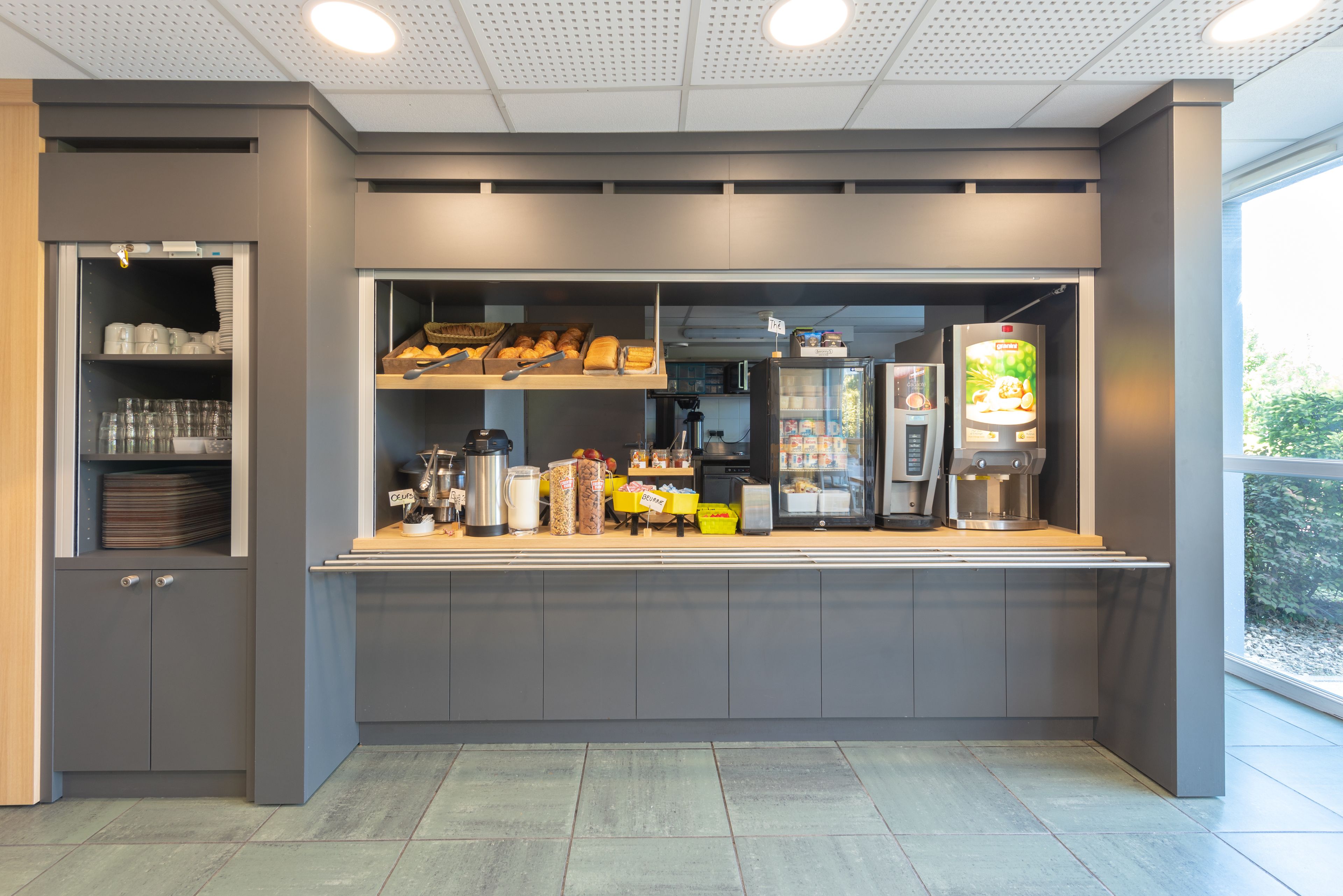 Un café moderne avec un comptoir, des étagères remplies de produits de boulangerie, une machine à café et un présentoir réfrigéré.