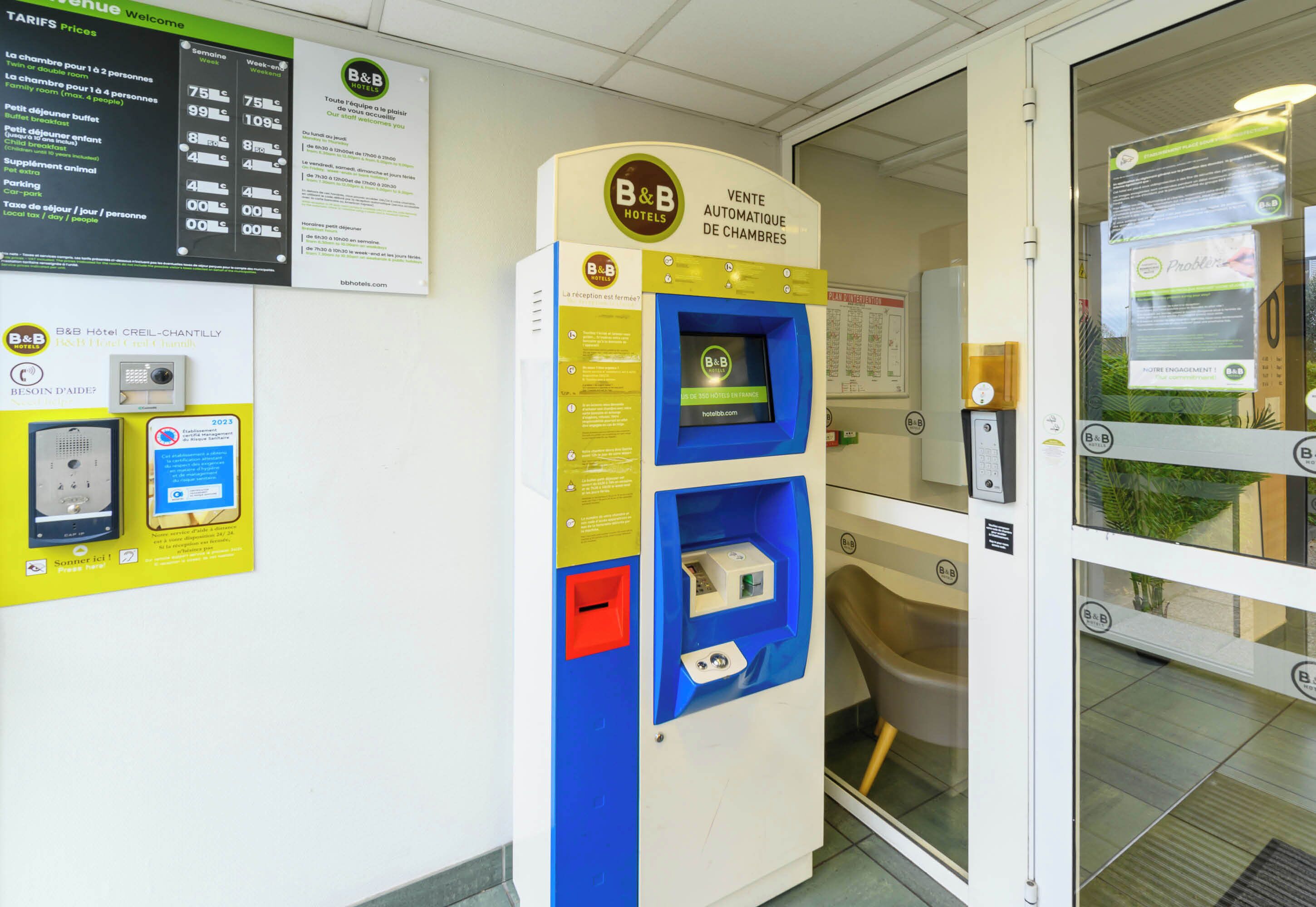 A B&B Hotel reception area with a self-service room booking machine, a wall-mounted information board, and a door with a glass panel.