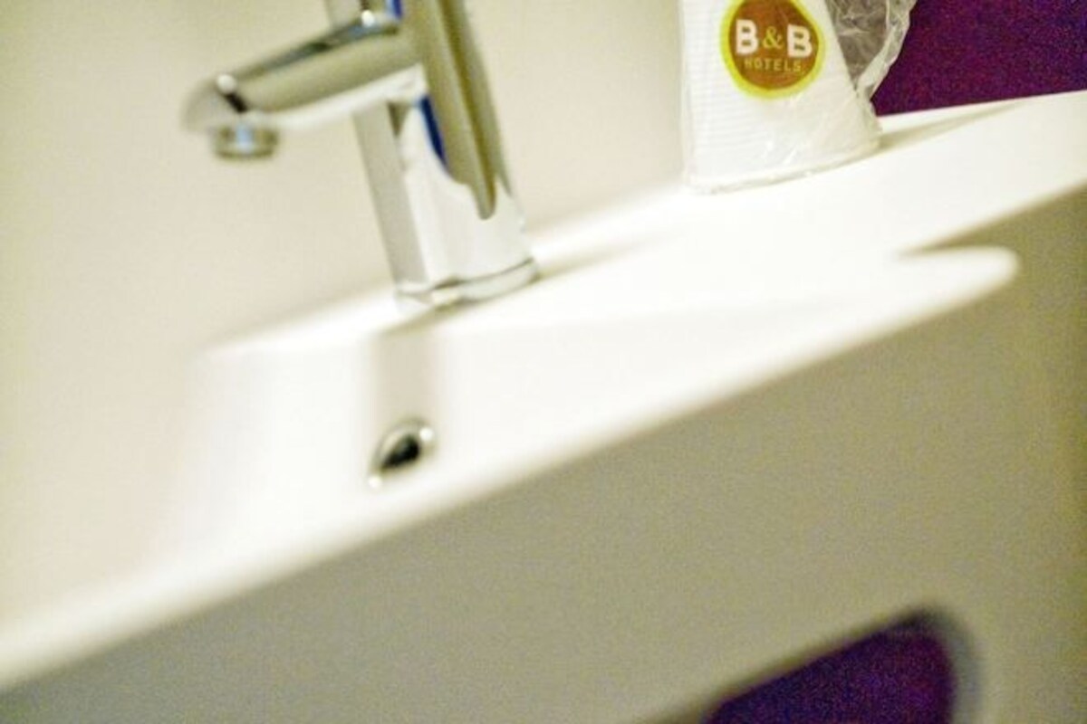 Ett handfat i badrummet med en blandare och en handduksdispenser från B&B Hotels.