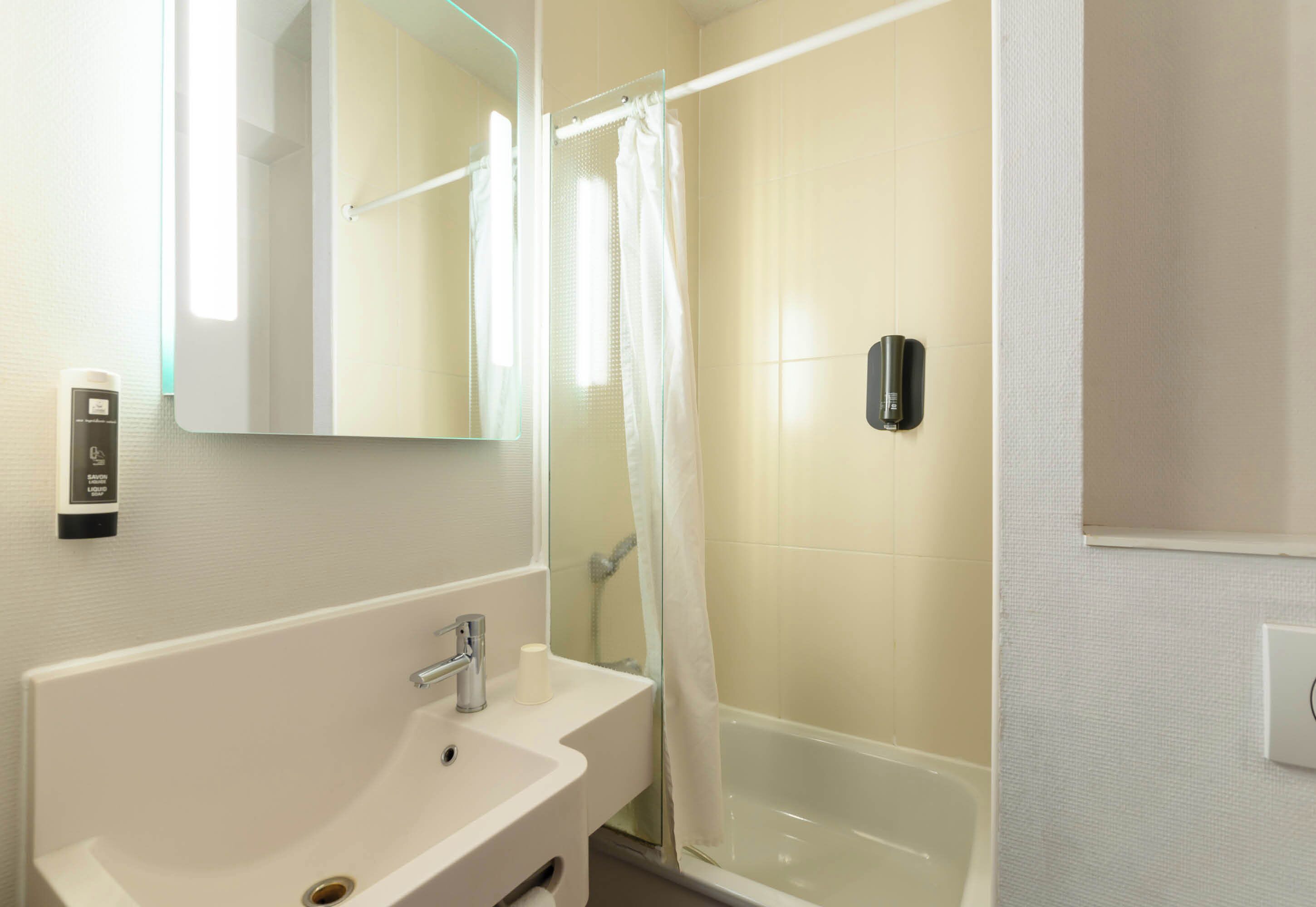 Un baño con un lavabo blanco, un espejo, una ducha con puerta de vidrio y un secador de manos.
