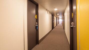 A hotel corridor with doors on both sides, a carpeted floor, and a yellow wall on one side.