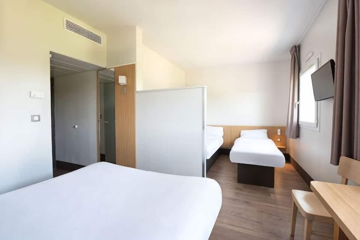Een hotelkamer met twee bedden, een bureau, een televisie en een deur naar een gang.