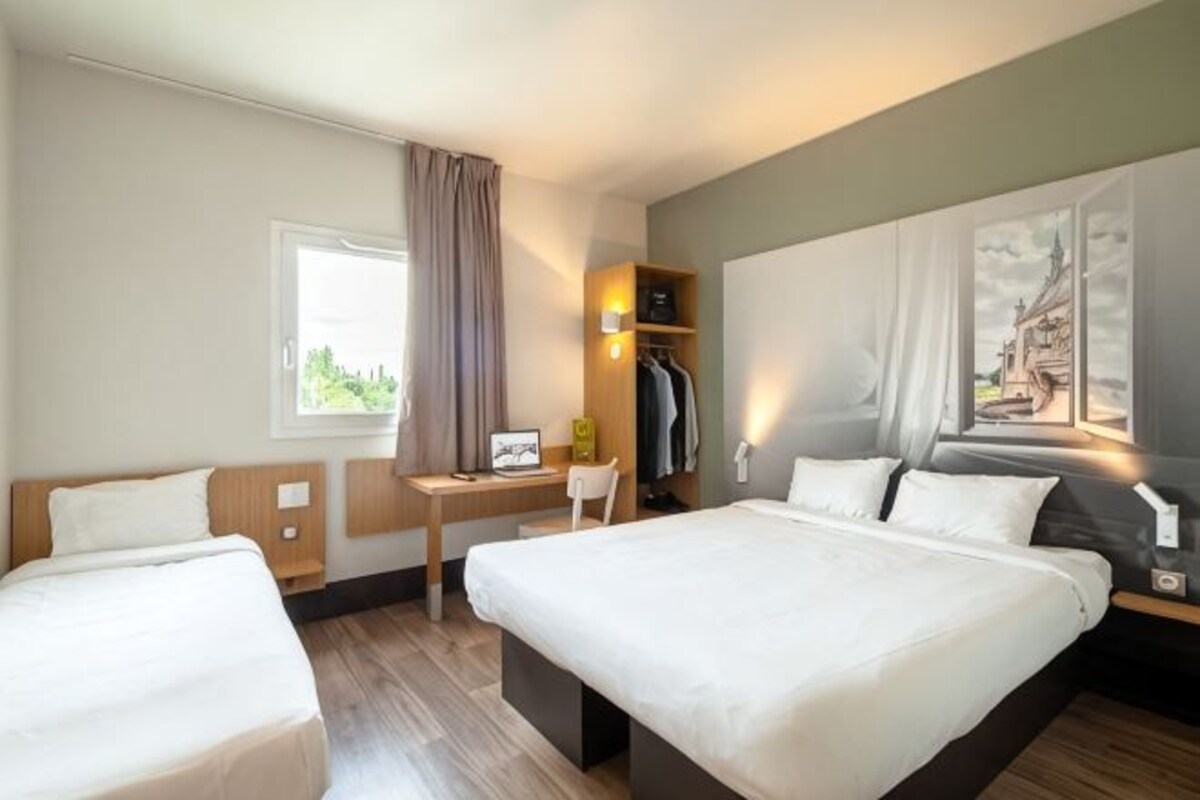 Ett hotellrum med två sängar, ett skrivbord, en stol, en garderob och ett fönster med gardiner.