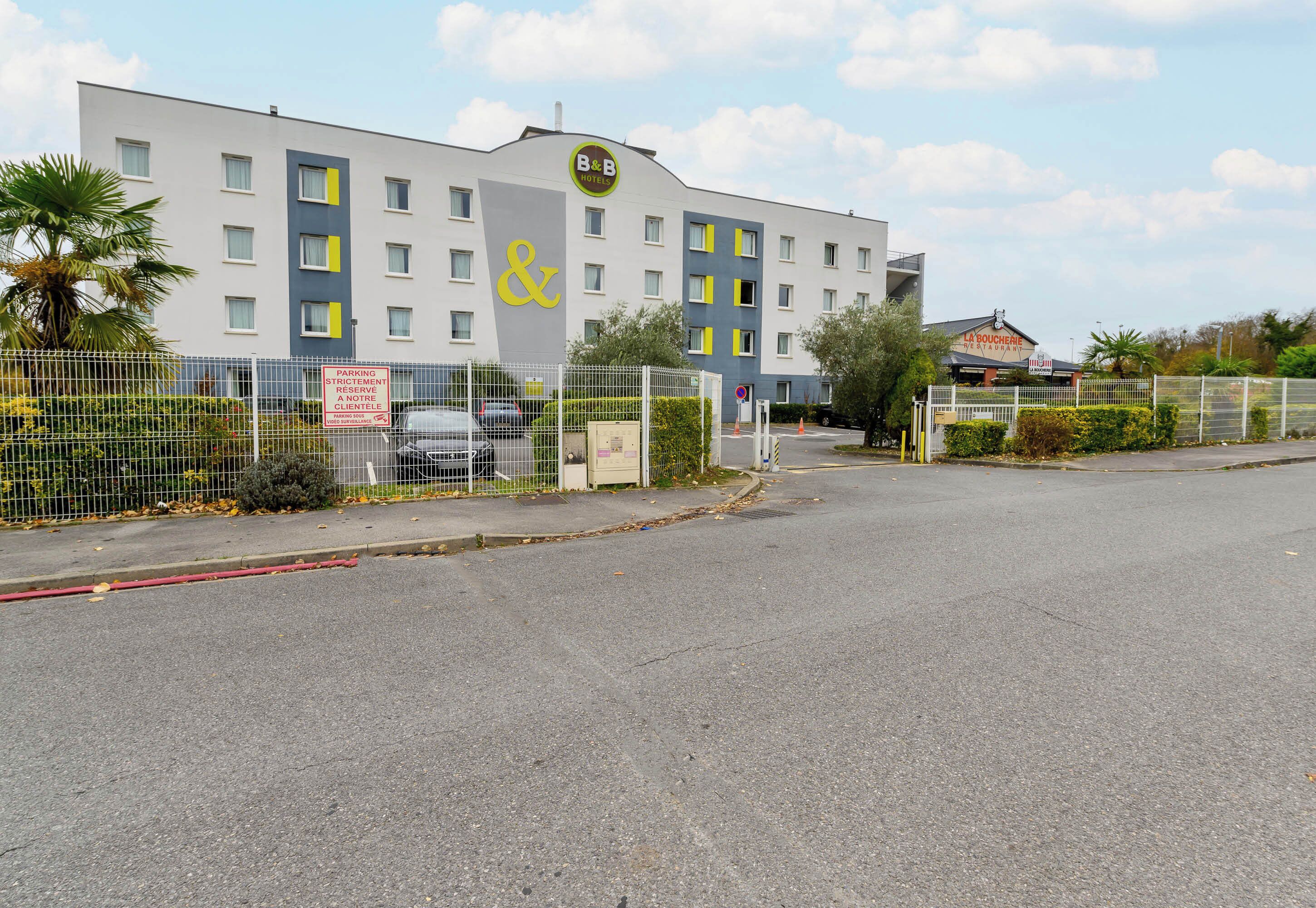 A B&B hotel with a modern facade, multiple floors, and a fenced parking area.