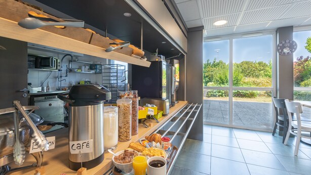 Un bufé de desayuno con recipientes etiquetados, una estación de café y vistas a zonas verdes al exterior.