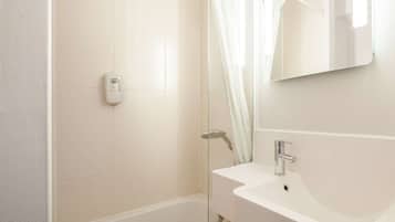 Une salle de bain moderne avec une douche à parois de verre, un lavabo blanc et un distributeur de savon portatif.