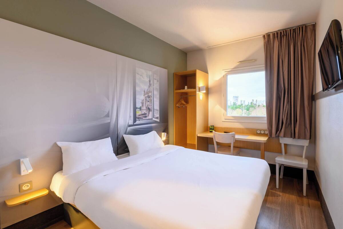 Een hotelkamer met een groot bed, een bureau, een stoel, een kledingkast en een televisie.