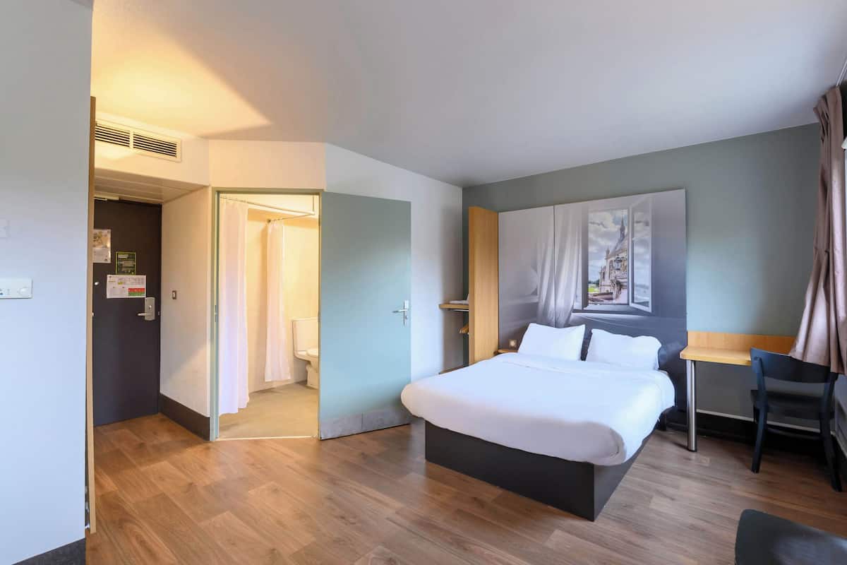 Een hotelkamer met een groot bed, een bureau, een stoel en een douchehoek.