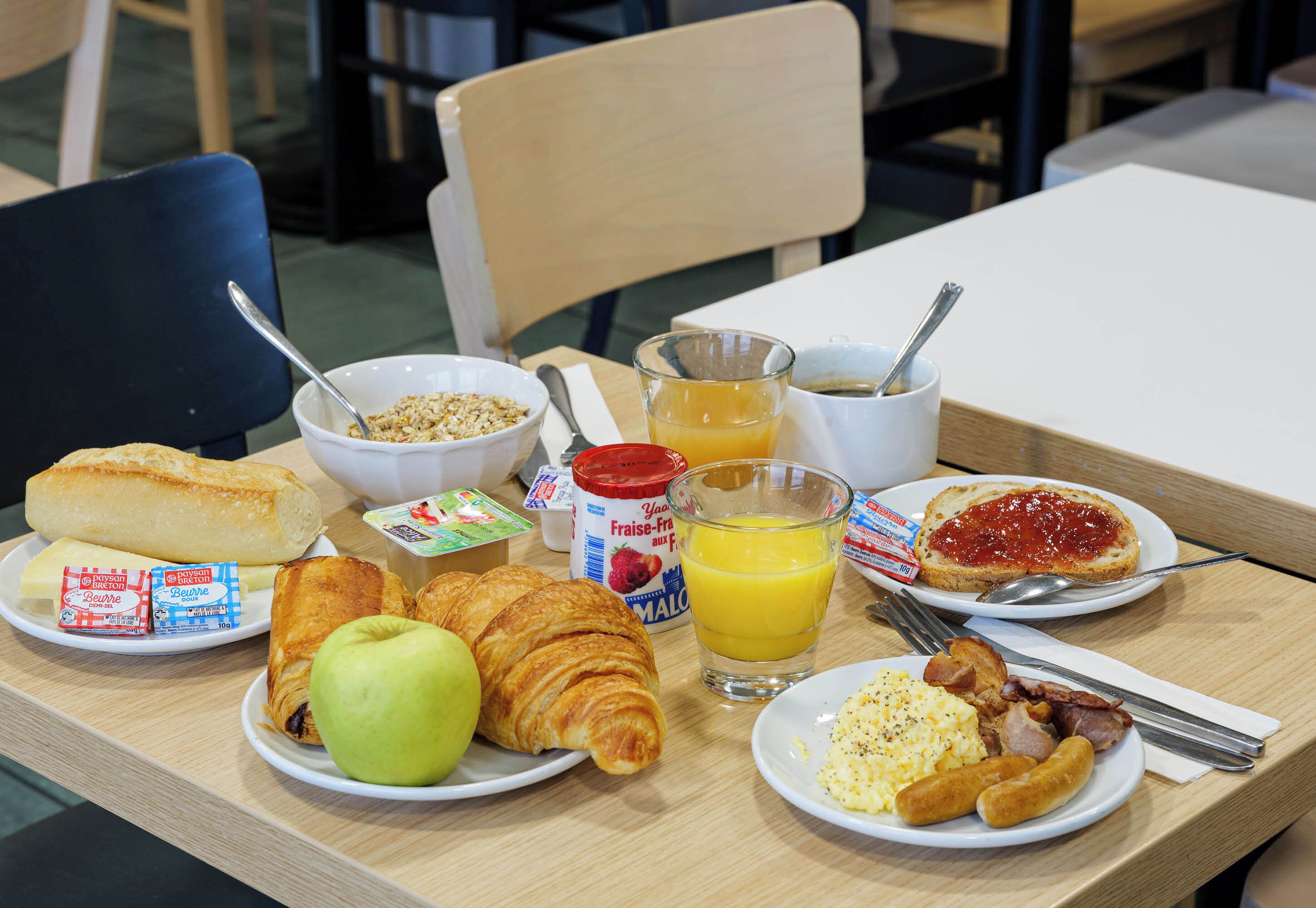 Una mesa de desayuno con cruasanes, una manzana, un vaso de zumo de naranja y diversas opciones para el desayuno.