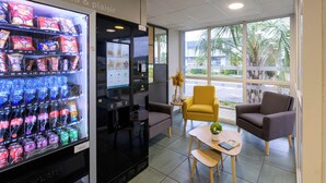 Un interior moderno con una máquina expendedora de bebidas, zona de estar y ventanas amplias.