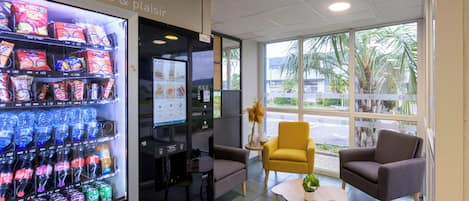 Un interior moderno con una máquina expendedora de bebidas, zona de estar y ventanas amplias.