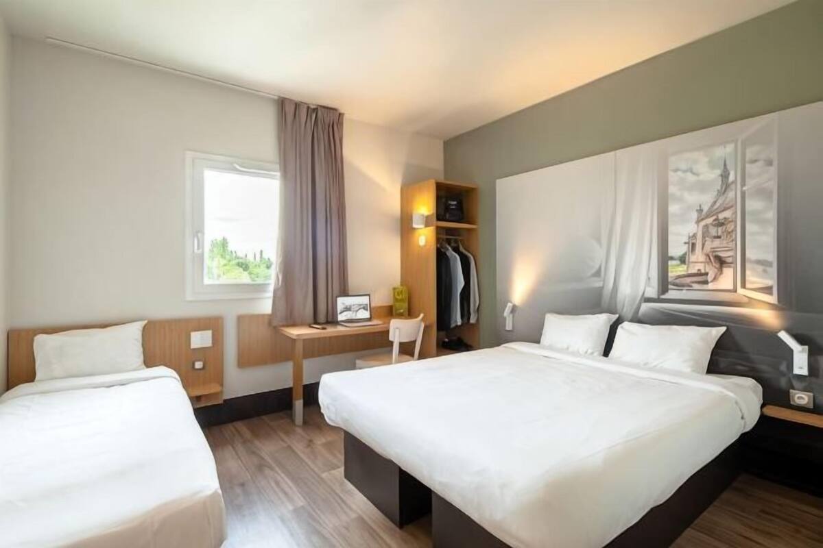 Een hotelkamer met twee bedden, een bureau, een stoel, een kledingkast en een raam met gordijnen.
