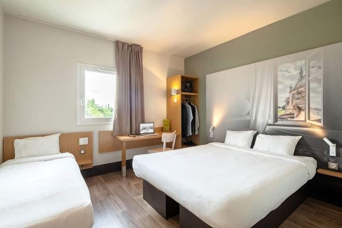 A hotel room with two beds, a desk, a chair, a wardrobe, and a window with curtains.