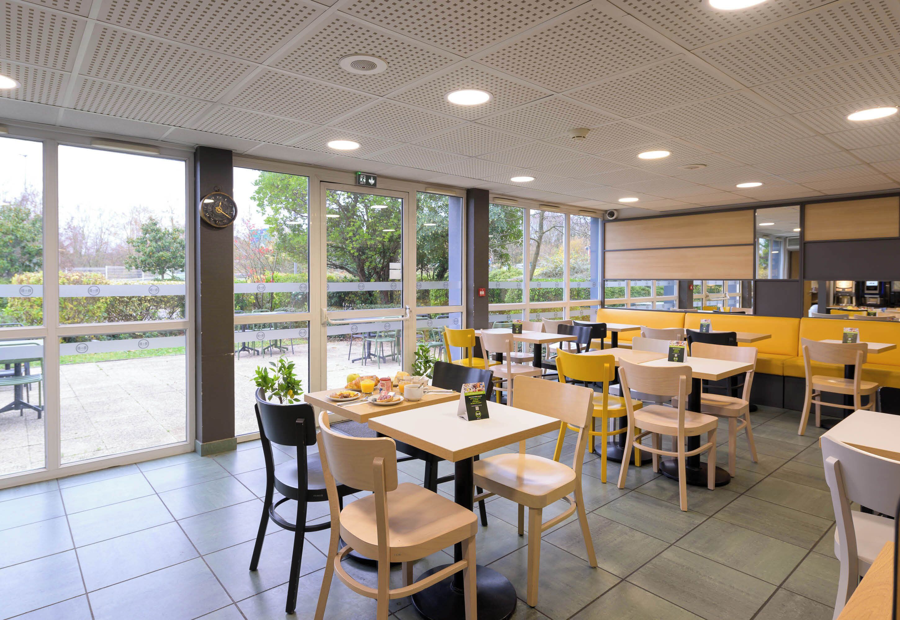 Een modern café met grote ramen, houten tafels en stoelen.