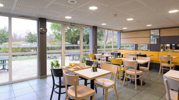 Een modern café met grote ramen, houten tafels en stoelen.