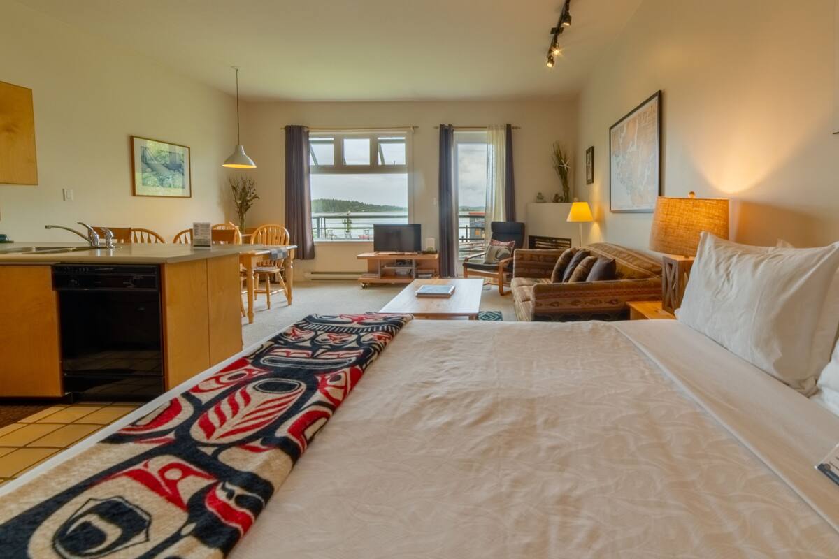 A hotel room with a bed, a desk, a chair, a sofa, and a view of the sea.