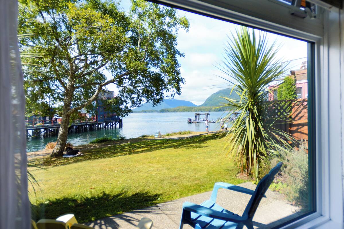 A view of a lake with a dock, a tree, and a chair in the foreground.