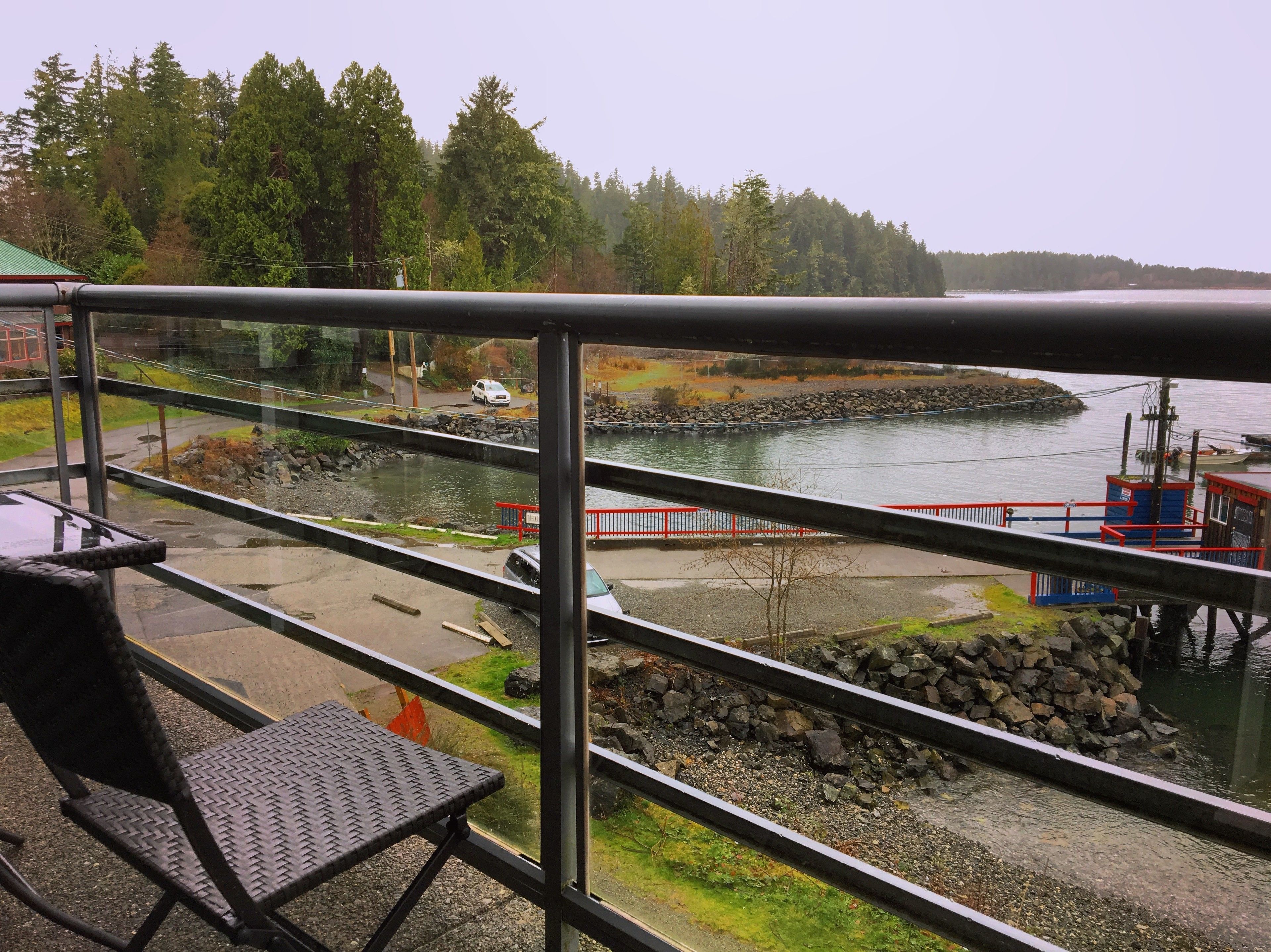 A balcony with a view of a river, a dock, and a forested area.