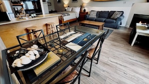 Un salon moderne comprenant un coin repas, une cuisine et une planche de surf accrochée au mur.