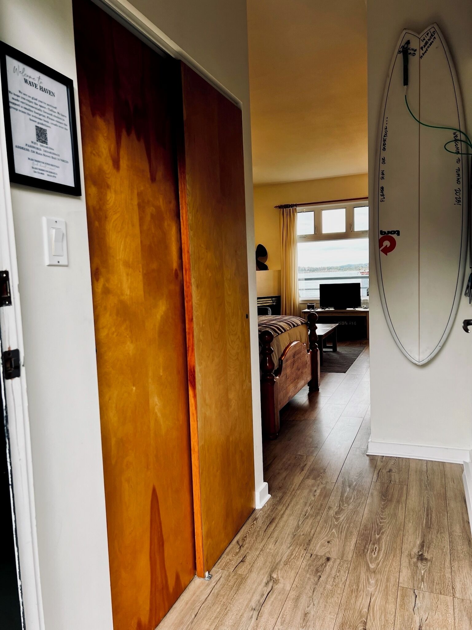 Una stanza con una porta in legno, un letto, una TV e una tavola da surf appesa al muro.