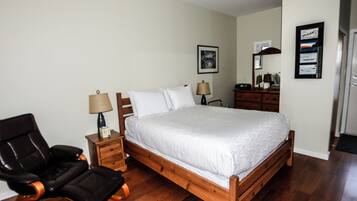 A bedroom with a wooden bed, a black leather chair, a nightstand with a lamp, and a dresser with a mirror.
