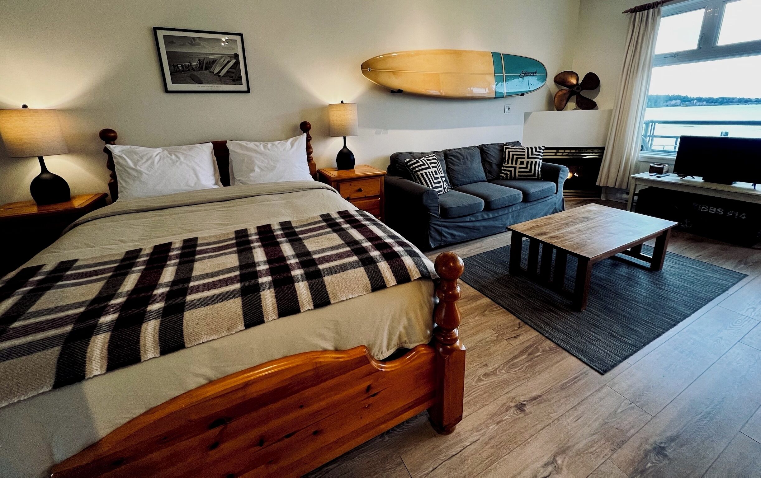 A hotel room with a bed, a sofa, a coffee table, a TV, and a surfboard on the wall.