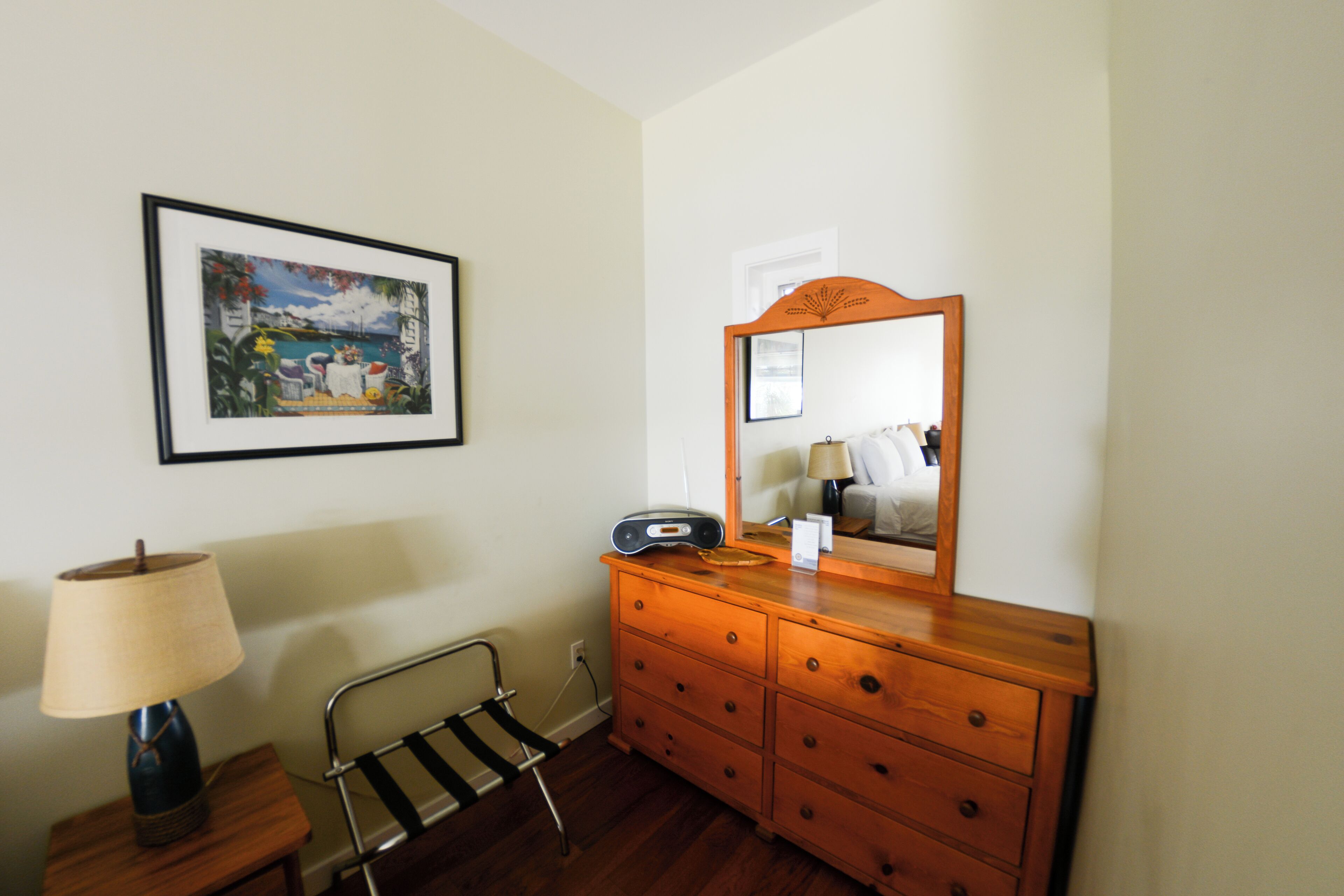 Une pièce avec une commode en bois, un tableau encadré au mur, une lampe et une chaise.