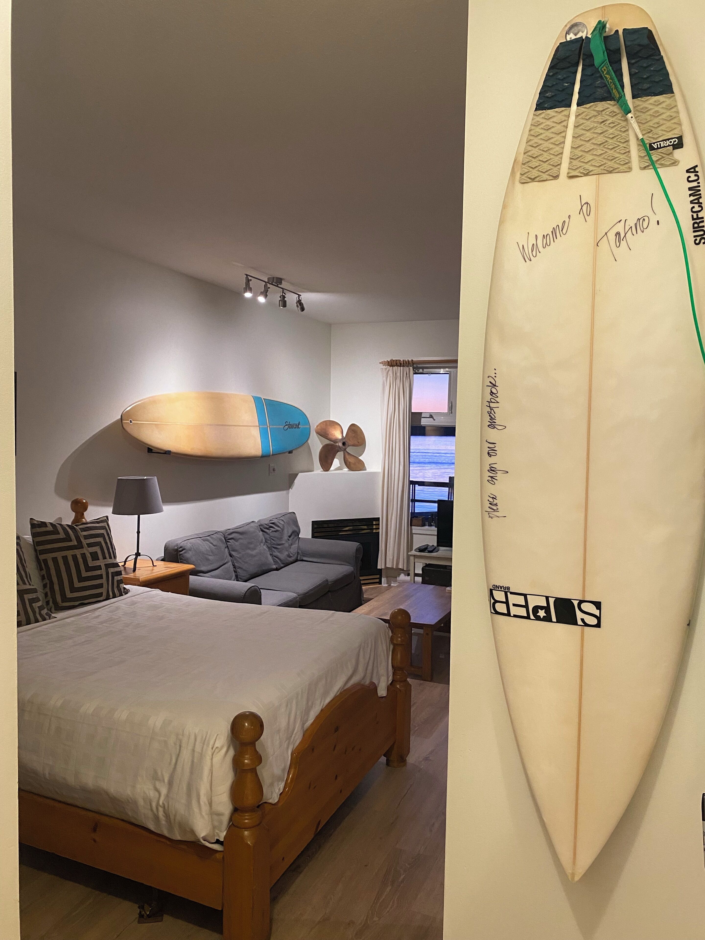 Ein Schlafzimmer mit einem Bett, einem Schlafsofa, einem Schreibtisch und einem Surfbrett an der Wand.