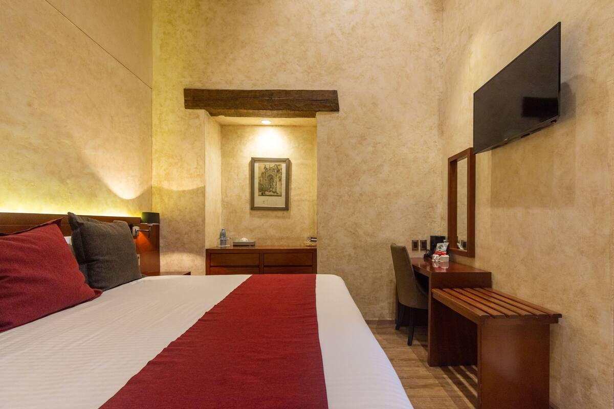A hotel room with a large bed, a desk, a chair, a flat-screen TV mounted on the wall, and a framed picture on the wall.