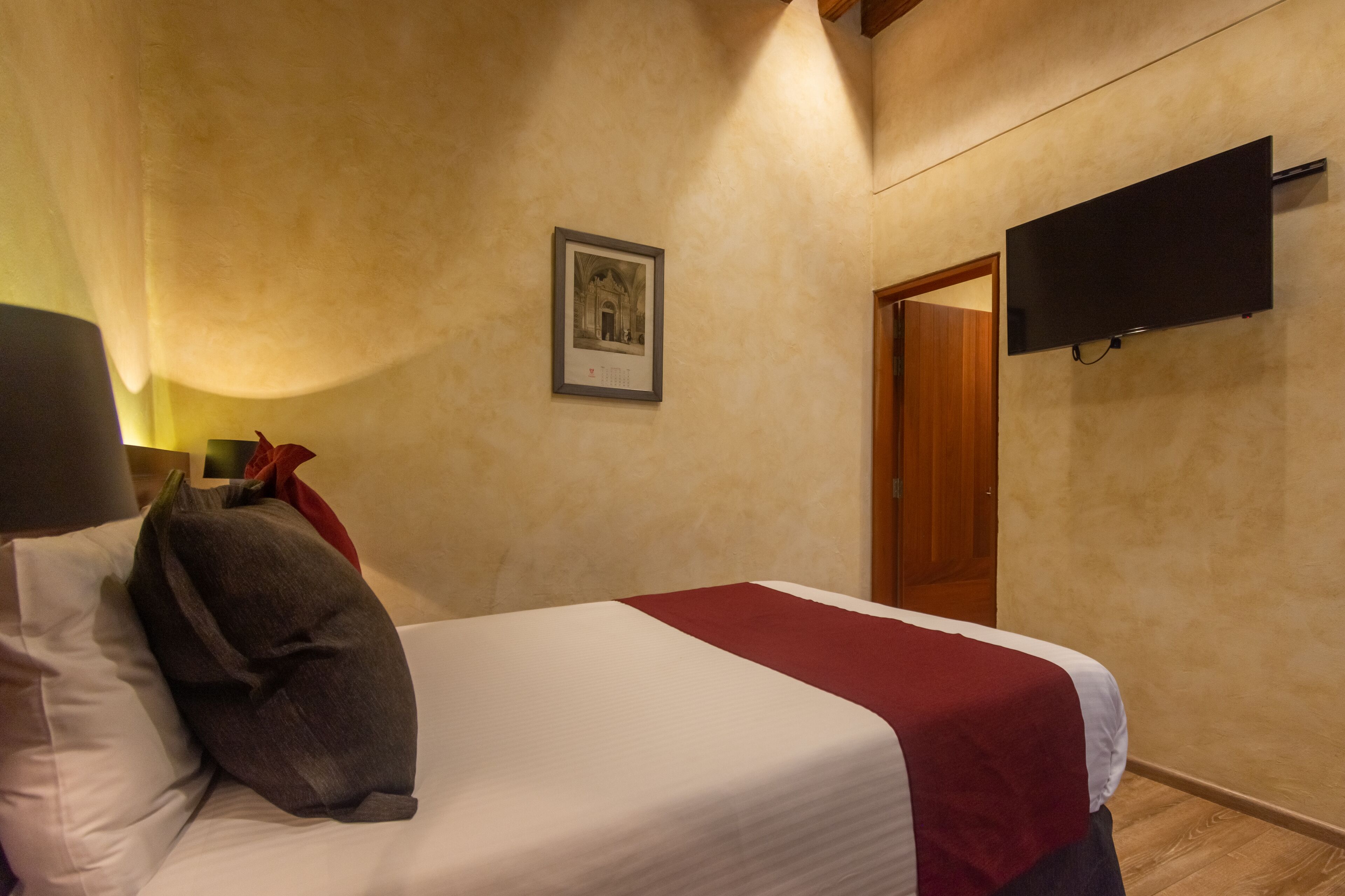A hotel room with a bed, a TV mounted on the wall, and a framed picture on the wall.