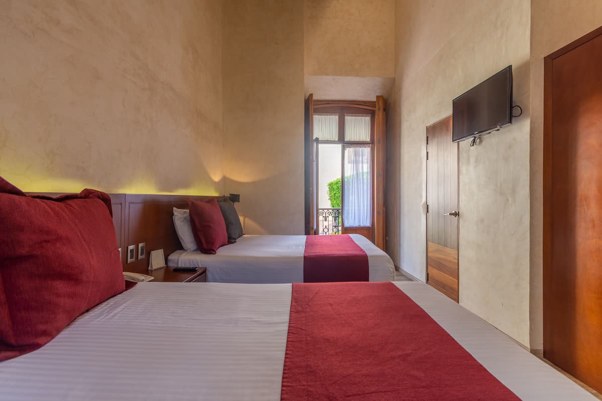 A hotel room with two beds, a TV mounted on the wall, and a balcony with a view.