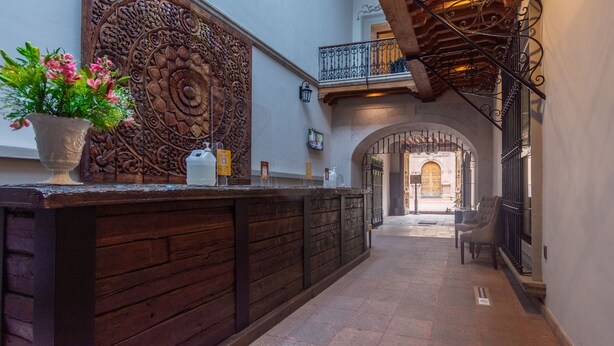 Un pasillo estrecho con un mostrador de recepción de madera, un muro decorativo y vista a un patio.