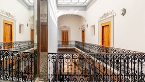 Un amplio pasillo con tragaluces, barandillas ornamentales y puertas de madera.